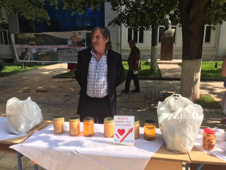 Prodhues mjalti pranë tavolinës me kavanoza mjalti në një panair